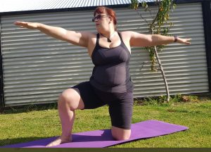 woman in a garden with arms outstretched kneeling down in a yoga pose.