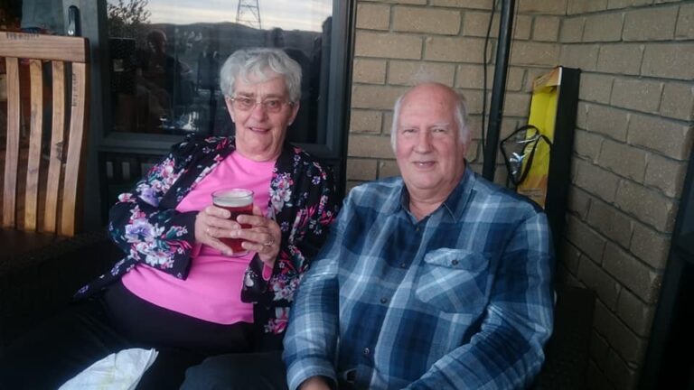 Older man and woman couple smile at the camera holding drinks.