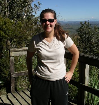 A woman at a lookout in the bush smiling against a blue sky.